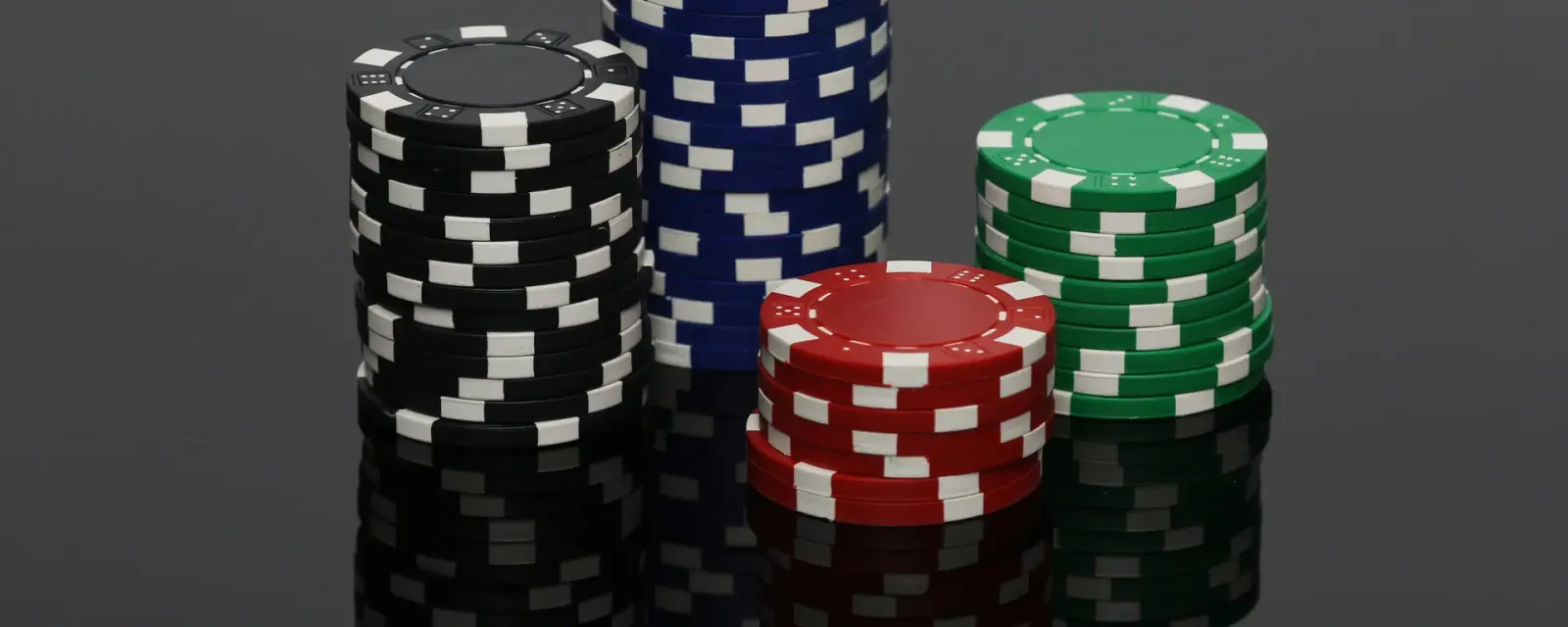 Black, blue, red and green poker chip stacks reflected on a grey surface